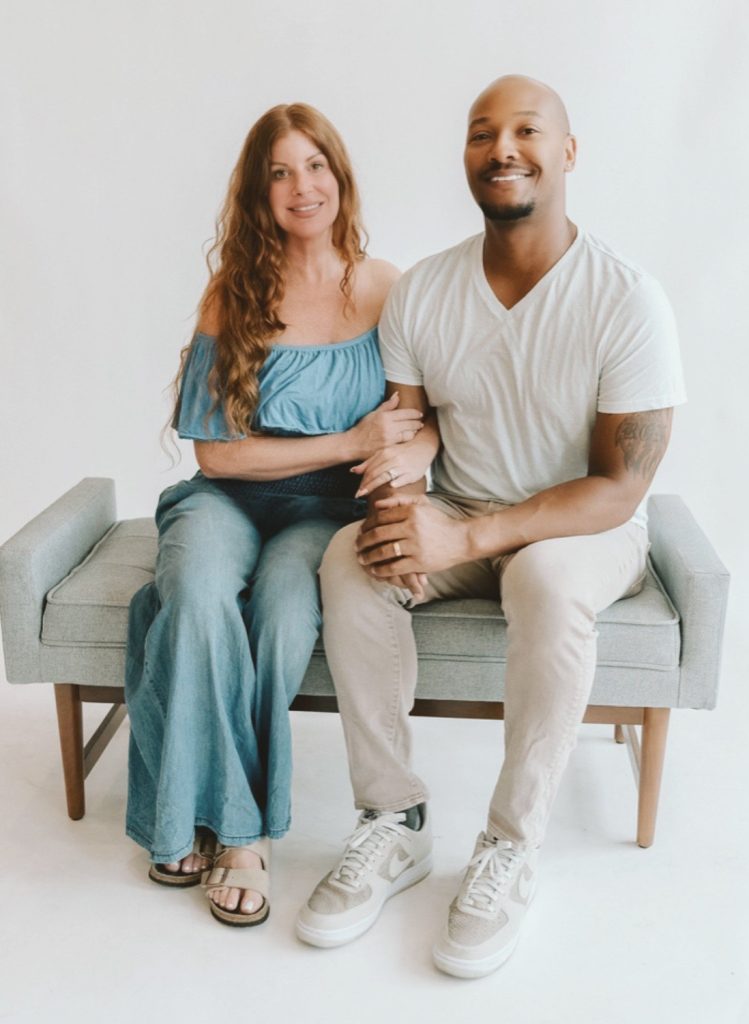 Ron and Angela Tabb together on a gray bench against a white background, holding hands.