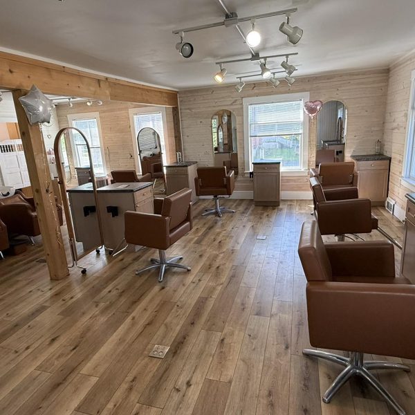 Modern hair salon with brown chairs, large mirrors, wood floors, and plenty of natural light from windows.