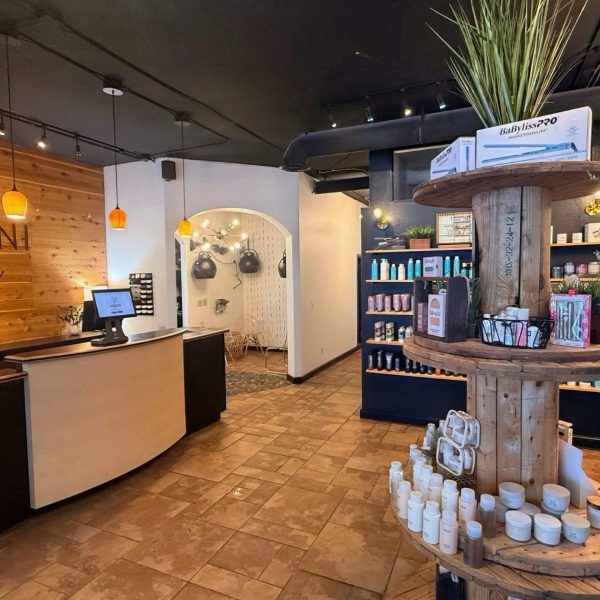 Modern salon interior with wooden accents, product shelves, and a curved front desk; plants add a fresh touch.