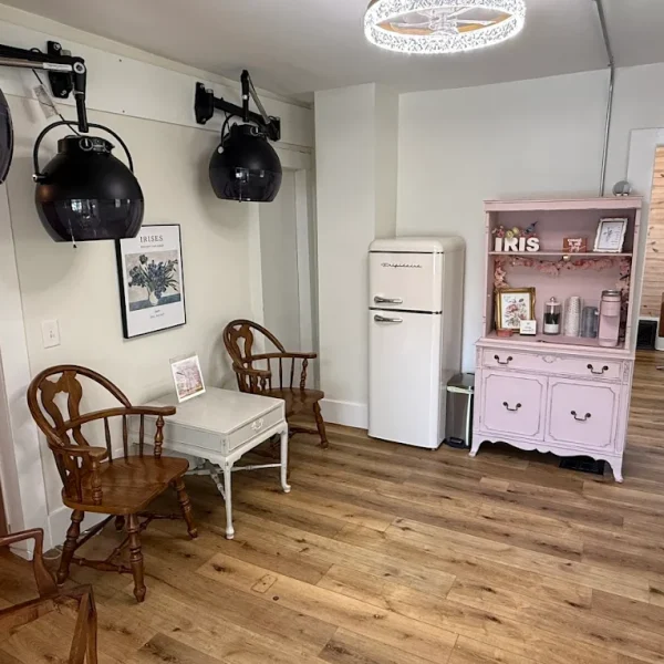 Small vintage-style salon room with wooden chairs, old-fashioned dryers, and a pink cabinet on wooden floors.